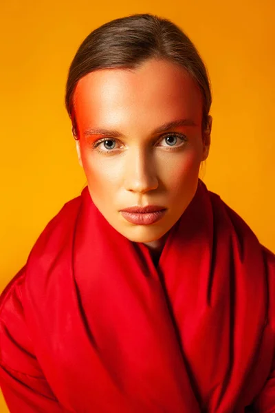 Young woman wrapping in red coat against yellow background — Stock Photo, Image