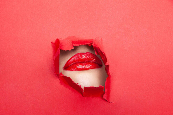Woman with red lips through torn paper