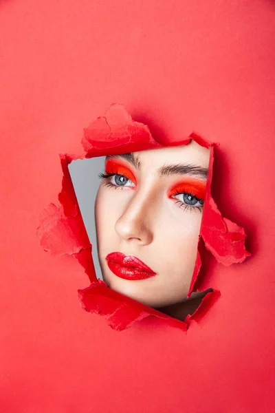 Mulher com visagem vermelha olhando através de papel rasgado — Fotografia de Stock