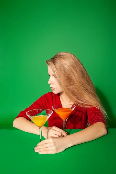 Mladá žena odpočívá v blízkosti barevné koktejly na zeleném pozadí — Stock fotografie