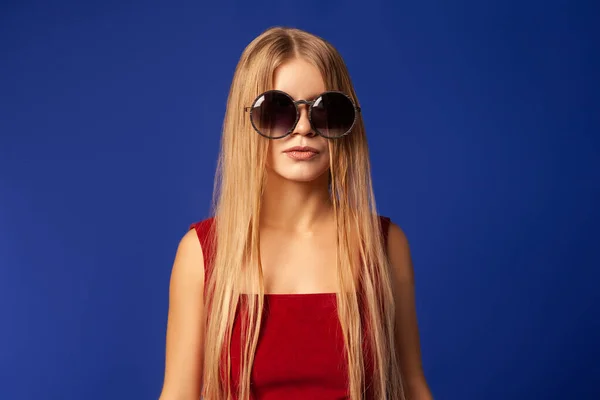 Junge Frau mit trendiger Sonnenbrille auf blauem Hintergrund — Stockfoto