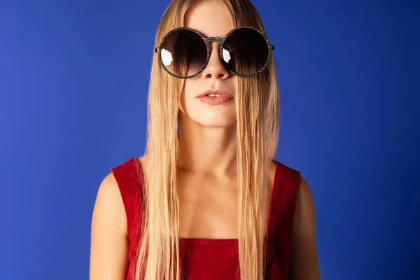 Jeune femme en lunettes de soleil à la mode sur fond bleu — Photo