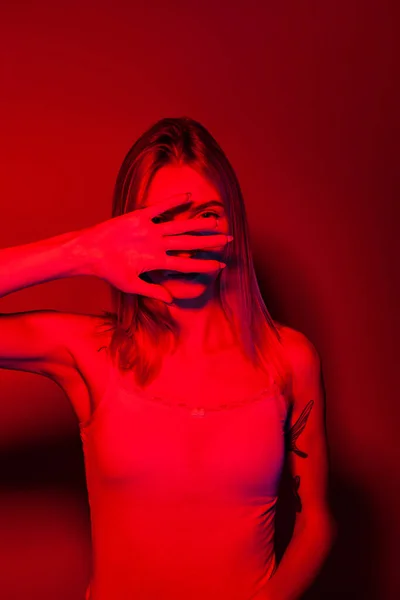 Donna anonima che copre il viso con la mano in luce rossa al neon — Foto Stock