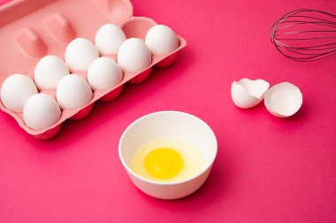 Yumurta kutusu yumurta sarısı kasesinin yanında ve pembe masada çırpın.