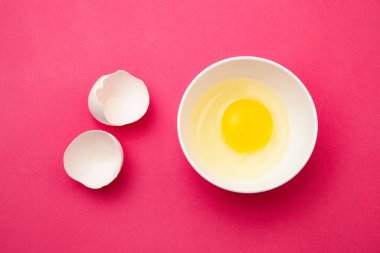 Pembe yüzeyde, kabuğun yanında kırık yumurta var.