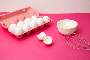 Yumurta kutusu yumurta sarısı kasesinin yanında ve pembe masada çırpın.