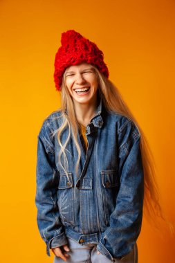 Parlak turuncu arka planda kalın giysiler içinde gülümseyen genç kadın.