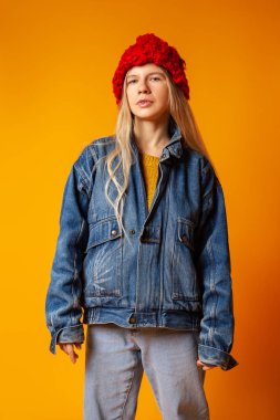 Parlak turuncu arka planda kalın giysiler içinde gülümseyen genç kadın.