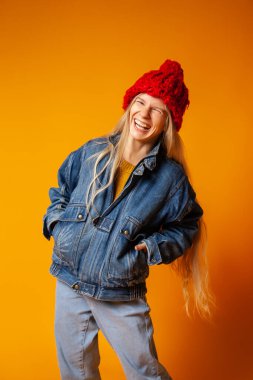 Parlak turuncu arka planda kalın giysiler içinde gülümseyen genç kadın.