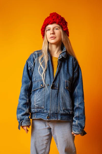 Parlak turuncu arka planda kalın giysiler içinde gülümseyen genç kadın.