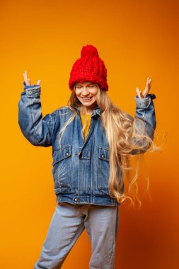 Parlak turuncu arka planda kalın giysiler içinde gülümseyen genç kadın.