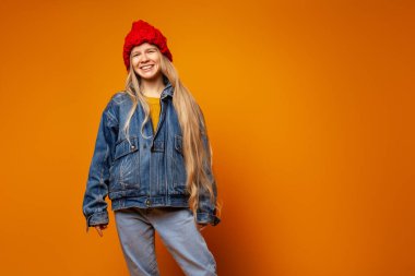 Parlak turuncu arka planda kalın giysiler içinde gülümseyen genç kadın.