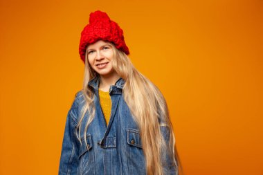 Parlak turuncu arka planda kalın giysiler içinde gülümseyen genç kadın.