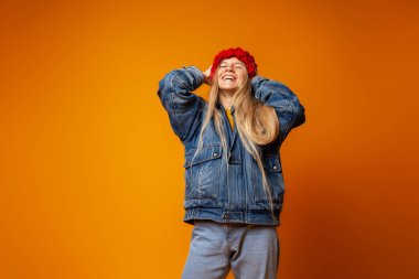 Parlak turuncu arka planda kalın giysiler içinde gülümseyen genç kadın.