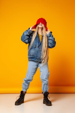 Kot elbiseli ve şapkalı neşeli moda kadın stüdyoda eğleniyor.