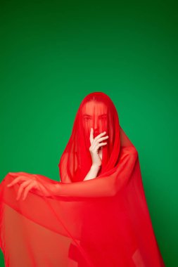 Yeşil arka planda kırmızı peçeli gizemli kadın.