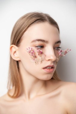 Beyaz arka planda yüzünde çiçekler olan genç bir kadın.