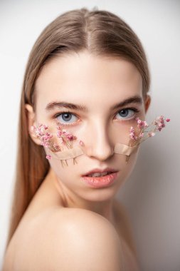 Beyaz arka planda yüzünde çiçekler olan genç bir kadın.