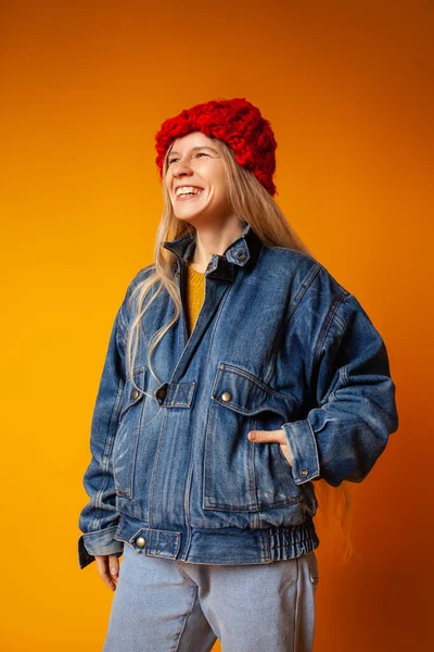 Parlak turuncu arka planda kalın giysiler içinde gülümseyen genç kadın.