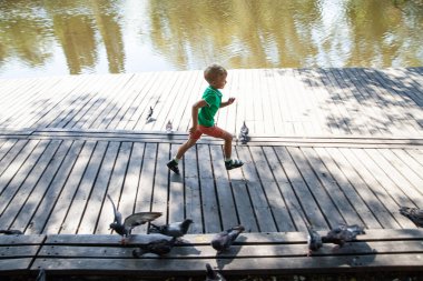 Küçük çocuk yaz günü tahta yolda koşuyor.