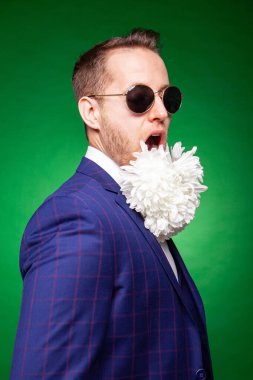 Boynunda çiçekler, atölyesinde takım elbiseli neşeli bir adam.