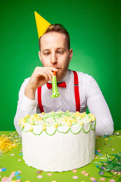 Man blowing party horn at table with birthday cake — Stock Photo, Image