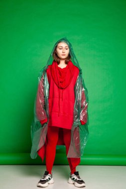 Stüdyoda yeşil arka planda duran yağmurluklu kadın.
