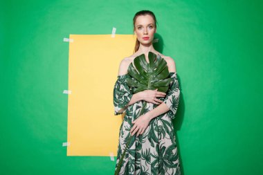 Yazlık elbise giymiş genç bir kadın yaprak tutuyor.