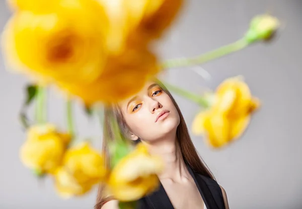 Mujer joven mirando la cámara detrás de la flor amarilla — Foto de Stock