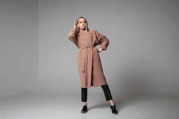Молодая женщина в элегантном пальто трогает волосы