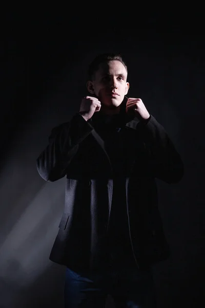 Stylowy mężczyzna w czarnym płaszczu w ciemnym studio — Zdjęcie stockowe