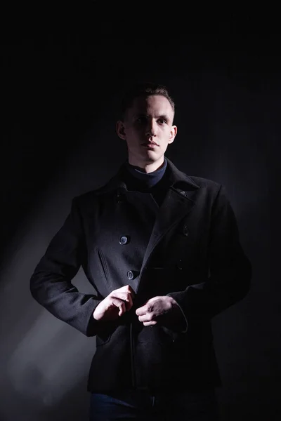 Stylish man in black coat in dark studio — Stock Photo, Image