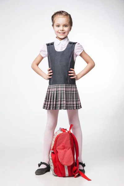 Ευτυχισμένος μικρή μαθήτρια σε ομοιόμορφη στέκεται πάνω σε λευκό φόντο Φωτογραφία Αρχείου