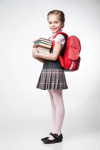 Ευτυχισμένος μικρή μαθήτρια σε ομοιόμορφη στέκεται πάνω σε λευκό φόντο Εικόνα Αρχείου