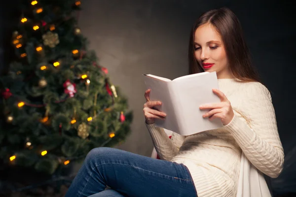 Woman in front of Christmas tree reading book — Stock Photo, Image