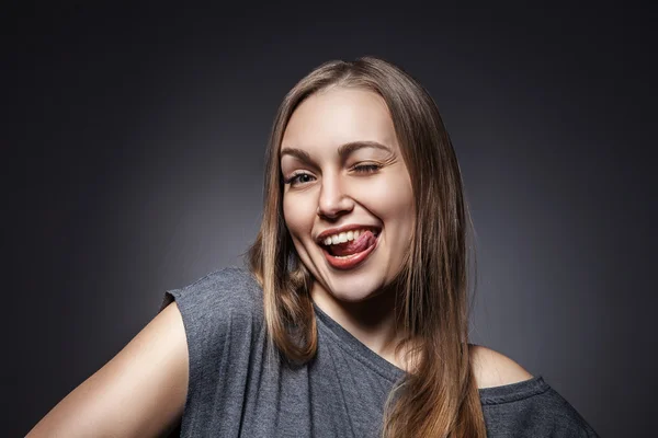 Glückliche Frau streckt ihre Zunge über Grau — Stockfoto