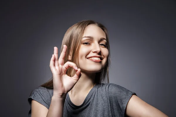 Smiling woman with okay gesture on dark grey — Stock Photo, Image