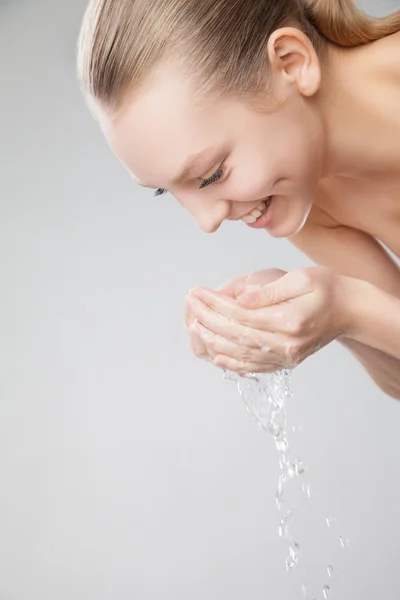 물으로 그녀의 깨끗 한 얼굴을 세척 하는 아름 다운 여자 — 스톡 사진