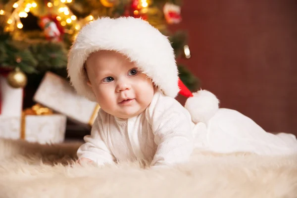 Happy baby wearing Santa hat over christmas tree — Stock Photo, Image