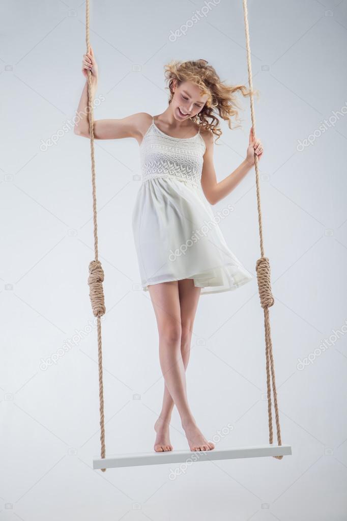 Young bare-footed girl on swing looking down.