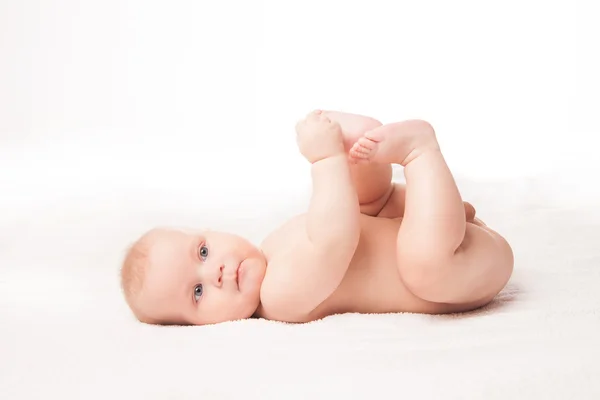 Bebê bonito deitado no cobertor branco tocando seus pés — Fotografia de Stock