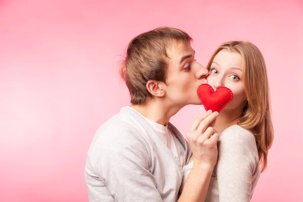 Homem beijando menina se escondendo atrás de um pequeno coração vermelho — Fotografia de Stock