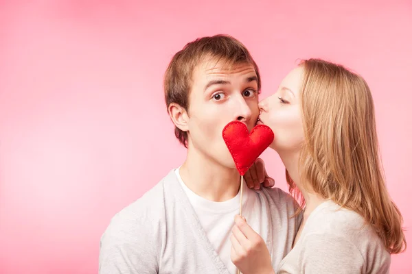 Meisje kussen jongen verstopt achter een beetje rood hart — Stockfoto