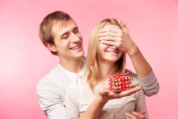 Man surprising woman with present over pink — Stock Photo, Image