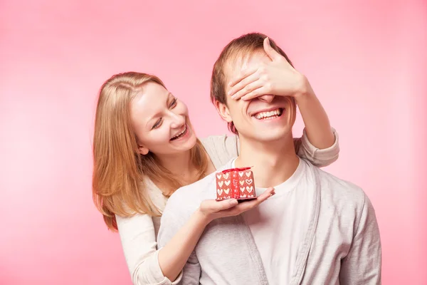 Woman surprising man with present over pink — Stock Photo, Image