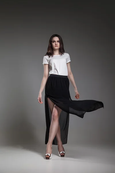 灰色の背景にポーズ白のトップと黒のスカートで美しいモデル — ストック写真