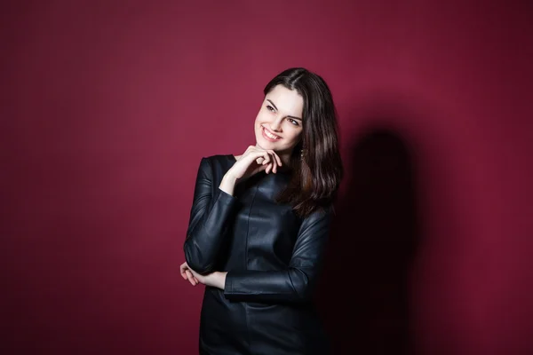 Retrato de jovem mulher bonita em vestido de couro no fundo vermelho — Fotografia de Stock