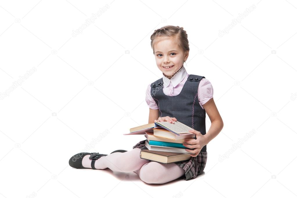 Beautiful little girl in school uniform with books sitting on the floor