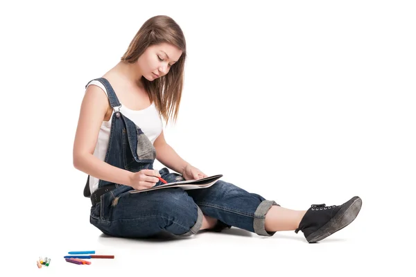 Молодая женщина счастливо сидит на полу рисуя в блокноте — стоковое фото