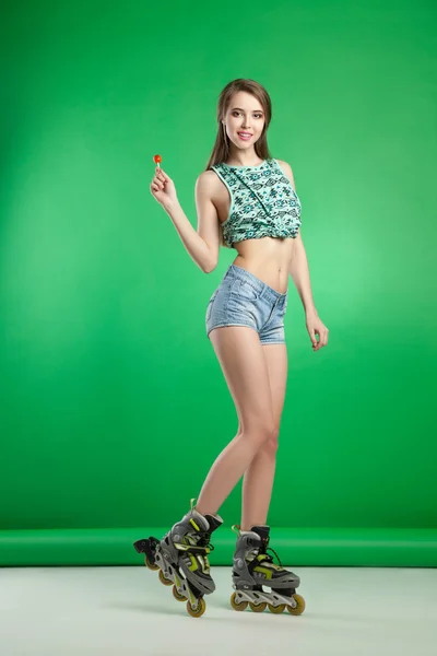 Zeer aantrekkelijke vrouw met lolly poseren op groene studio achtergrond dragen rollerskates — Stockfoto